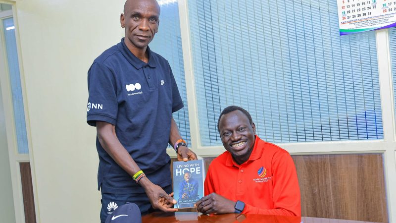 Eliud Kipchoge standing alongside Michael Panther of Hope Mobility Kenya holding a racing wheelchair.