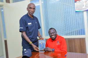 Michael Panther seated in a wheelchair presenting his book Living with Hope to Eliud Kipchoge.